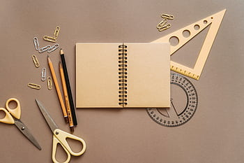 Flat lay of school supplies featuring a spiral notebook, scissors, and stationery on a brown background. HD wallpaper