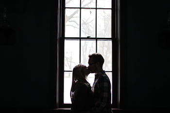 A romantic silhouette of a couple sharing a kiss in front of a large, backlit window. HD wallpaper