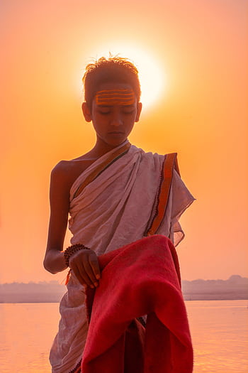 A young Indian priest performing a traditional ritual by the riverside in Varanasi at sunrise. HD phone wallpaper