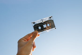 A person holds a vintage cassette tape against a clear blue sky, symbolizing nostalgia and technology. HD wallpaper