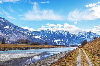 Explore the stunning Swiss Alps with a serene pathway alongside a flowing river under clear blue skies. HD wallpaper