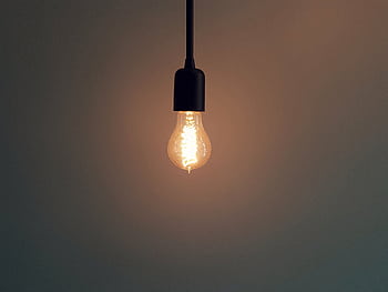 Simple illuminated light bulb hanging in a dark room, creating a warm atmosphere. HD wallpaper