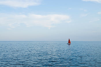 A lone sailboat with a red sail peacefully sailing on the open sea under a clear sky. HD wallpaper