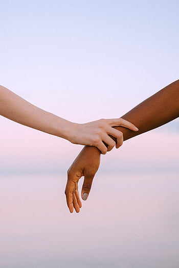 Close-up of two different skin toned hands holding gently against a serene sunset sky. HD phone wallpaper