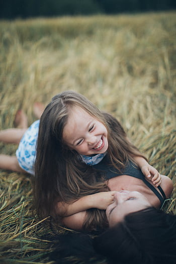 A joyful mother and daughter sharing a playful moment in a sunlit summer field. HD phone wallpaper