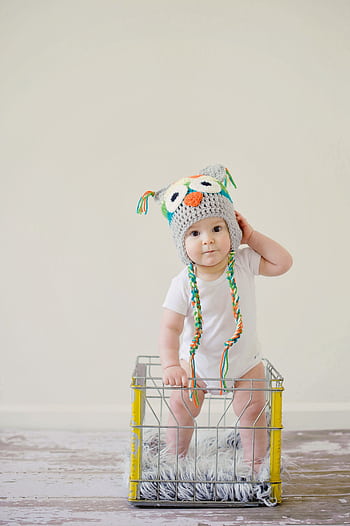 A cute baby wearing an owl hat standing in a basket, smiling and playful. HD phone wallpaper
