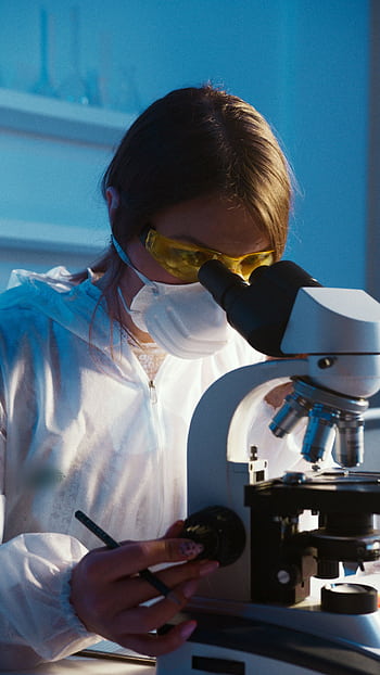 A female scientist examines a sample using a microscope in a laboratory setting. HD phone wallpaper