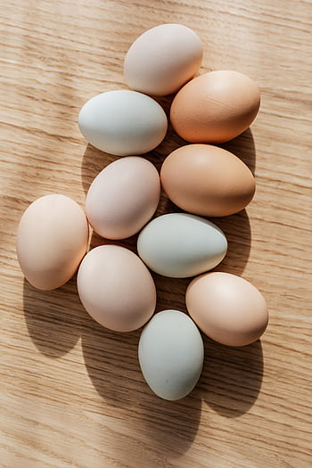 A collection of assorted eggs arranged on a sunlit wooden table. HD phone wallpaper