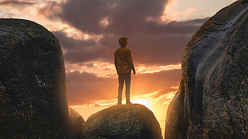 Boy Standing On A Boulder In Between Mountains, hoodie, alone, graphy, mountains HD wallpaper