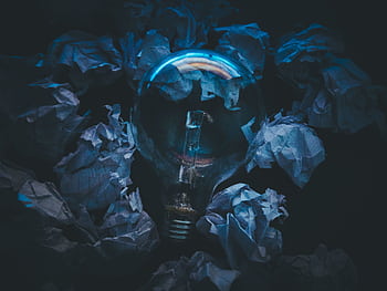 A light bulb surrounded by crumpled paper symbolizes creative ideas and innovation in a dark setting. HD wallpaper