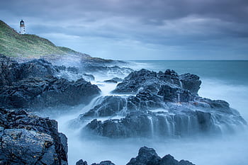 Captivating seascape of a lighthouse and rugged coastline with waves crashing against the rocks in Scotland. HD wallpaper