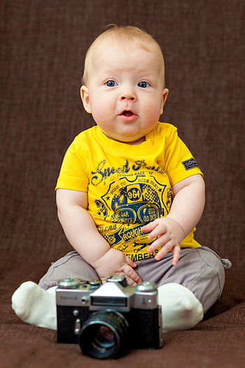 Charming baby boy in bright attire seated with a classic camera in a studio. HD phone wallpaper