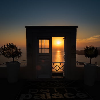 Stunning sunset view through a doorway in Santorini, Greece, with a serene seascape backdrop. HD phone wallpaper