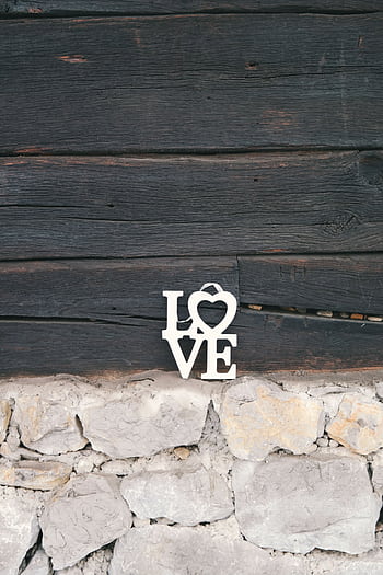 A charming love sign on a rustic wooden wall with stone base, perfect for romantic themes. HD phone wallpaper