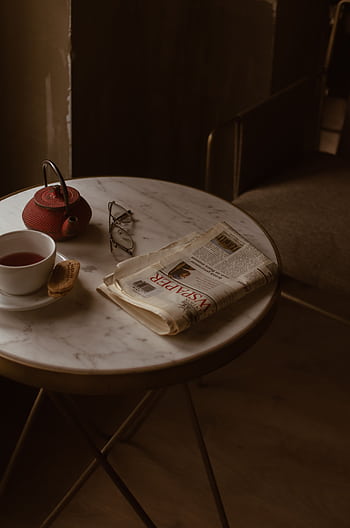 A cozy setup indoors with a cup of tea, newspaper, and glasses on a marble table. HD phone wallpaper