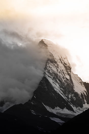 Dramatic view of snow-covered Matterhorn peak piercing clouds at sunrise in Zermatt, Switzerland. HD phone wallpaper