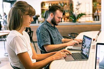 Two young professionals working on laptops in a modern cafe setting. HD wallpaper