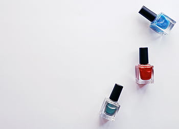 Three colorful nail polish bottles arranged creatively on a white backdrop, showcasing vibrant beauty products. HD wallpaper