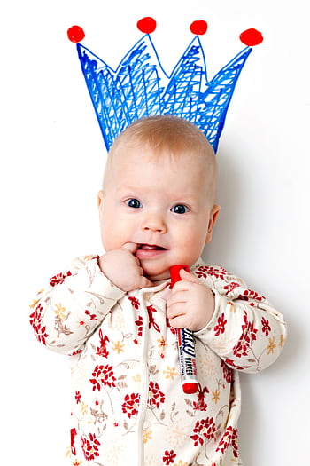 Cute baby wearing patterned clothing, holding a marker with a crown drawn above, exhibiting joy and innocence. HD phone wallpaper