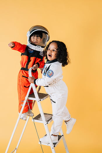 Joyful kids in astronaut suits playing on a ladder against a yellow background. HD phone wallpaper