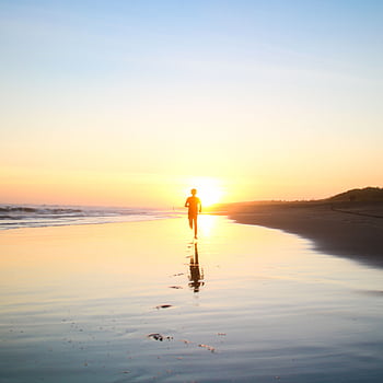 A lone silhouette of a person running along a serene beach at sunset, reflecting in the wet sand. HD phone wallpaper