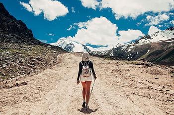 Back view of a woman hiking on a scenic mountain trail during daylight. HD wallpaper
