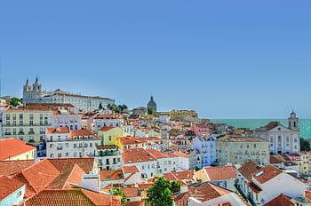Captivating view of Lisbon's historic architecture with the Atlantic Ocean in the backdrop under a clear blue sky. HD wallpaper
