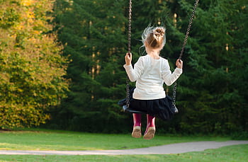 Young girl swinging in the park, surrounded by lush greenery on a sunny day. HD wallpaper