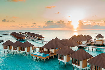 Discover the serenity of overwater bungalows at sunrise, offering a luxurious tropical escape. HD wallpaper