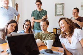 A diverse group of adults at work, enjoying a casual meeting indoors with focus and smiles. HD wallpaper