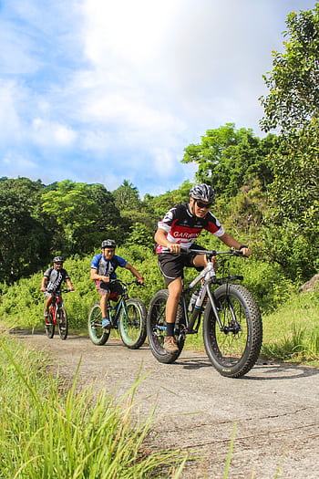Three cyclists enjoy mountain biking through lush greenery in Batangas, Philippines. HD phone wallpaper
