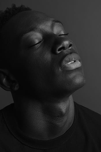 Emotive black and white portrait of a young man, eyes closed, in a studio setting. HD phone wallpaper