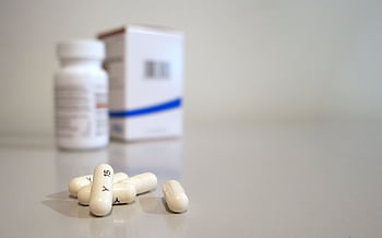 Close-up of white capsules with medicine bottle and box in the background. HD wallpaper