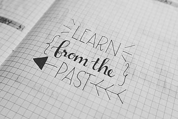 Black and white close-up of a handwritten motivational quote 'Learn from the Past' on graph notebook paper. HD wallpaper