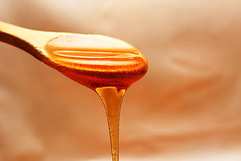 Close-up of honey dripping from a wooden spoon, showcasing its rich texture and color. HD wallpaper