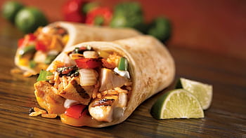 Close-up of a savory chicken burrito with fresh lime wedges, showcasing vibrant Mexican ingredients. HD wallpaper