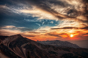 Stunning sunset over rugged mountains with dramatic clouds, capturing nature's beauty. HD wallpaper