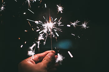 A hand holding a sparkler glowing brilliantly in the night, perfect for festive and holiday themes. HD wallpaper