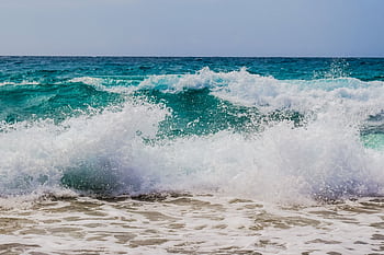 Dynamic ocean waves crashing onto a sandy shore under daylight, showcasing nature's power and beauty. HD wallpaper