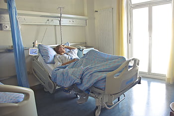 A woman lying in a hospital bed in a bright, softly lit room, appearing to rest or recover. HD wallpaper