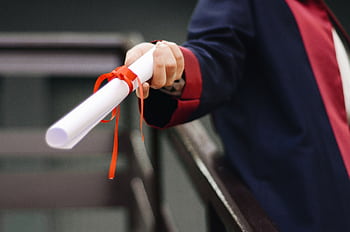 A close-up of a graduate holding a diploma tied with a red ribbon, symbolizing achievement and success. HD wallpaper