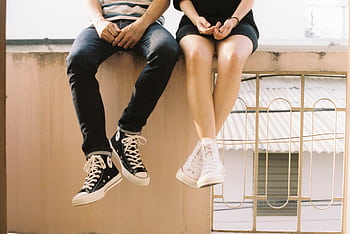 A relaxed couple sitting on a ledge, wearing stylish sneakers, showcasing togetherness. HD wallpaper