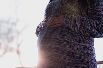 Close-up of a pregnant woman in a cozy sweater gently holding her belly, symbolizing motherhood. HD wallpaper