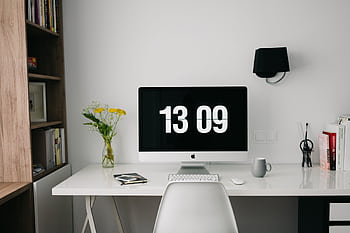 A minimalist workspace featuring a computer displaying time, organized bookshelves, and stylish decor. HD wallpaper