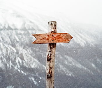 A wooden arrow signpost points the way amidst a snowy mountain landscape. HD wallpaper