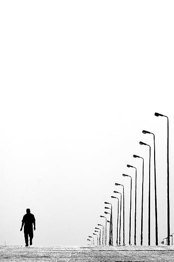 Silhouette of a man walking along a row of lampposts on an empty road in black and white. HD phone wallpaper