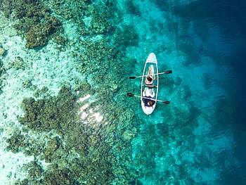 Aerial view of clear canoe gliding over vibrant coral reefs in the Maldives' turquoise waters. HD wallpaper
