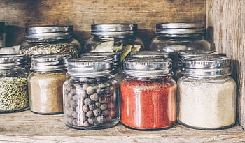 A collection of assorted spices in glass jars on a rustic wooden shelf for culinary use. HD wallpaper