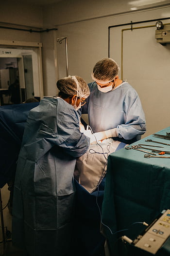 Two surgeons in an operating room conducting surgery under bright lights. HD phone wallpaper