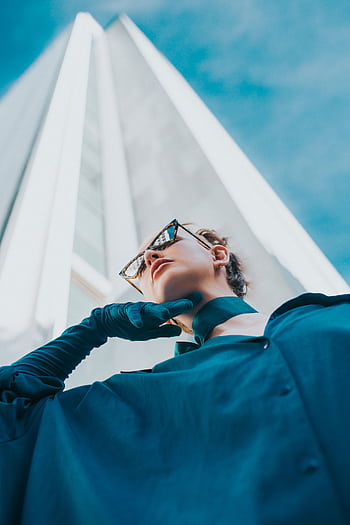 A fashion model in blue poses against a modern skyscraper under a bright blue sky in Portland. HD phone wallpaper